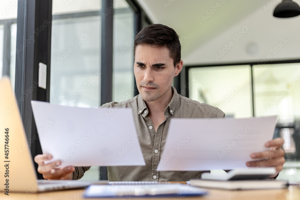 A businessman holding a sales document that the sales department summarizes, he looks displeased when he sees reports of falling sales, he shows signs of stress. Failed sales management concept. A businessman holding a sales document that the sales department summarizes, he looks displeased when he sees reports of falling sales, he shows signs of stress. Failed sales management concept.