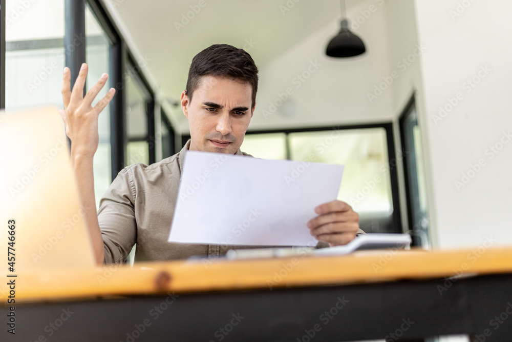 A businessman holding a sales document that the sales department summarizes, he looks displeased when he sees reports of falling sales, he shows signs of stress. Failed sales management concept. A businessman holding a sales document that the sales department summarizes, he looks displeased when he sees reports of falling sales, he shows signs of stress. Failed sales management concept.