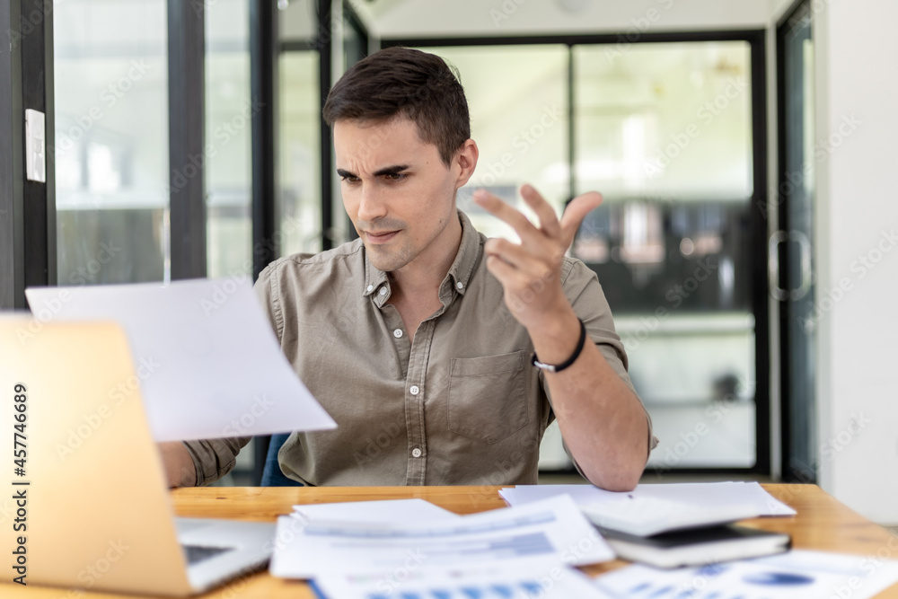 A businessman holding a sales document that the sales department summarizes, he looks displeased when he sees reports of falling sales, he shows signs of stress. Failed sales management concept. A businessman holding a sales document that the sales department summarizes, he looks displeased when he sees reports of falling sales, he shows signs of stress. Failed sales management concept.