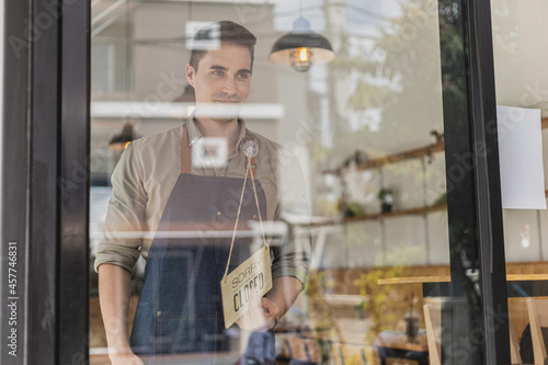 Handsome man holding a sign in front of a shop, a café employee standing holding a sign saying open-close, he's flipping a sign saying "closed". Cafe food and beverage service concept.