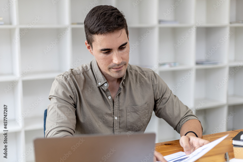 A young businessman sitting in the office working with a laptop, he is checking financial documents, he founded a startup, he is a young entrepreneur who has the skills to run a growing company. A young businessman sitting in the office working with a laptop, he is checking financial documents, he founded a startup, he is a young entrepreneur who has the skills to run a growing company.
