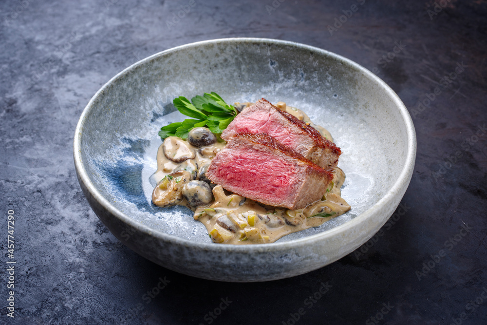 Modern style traditional barbecue dry aged angus roast beef steak natural with mushrooms and onions in cream sauce served as close-up in a Nordic design plate with copy space Modern style traditional barbecue dry aged angus roast beef steak natural with mushrooms and onions in cream sauce served as close-up in a Nordic design plate with copy space