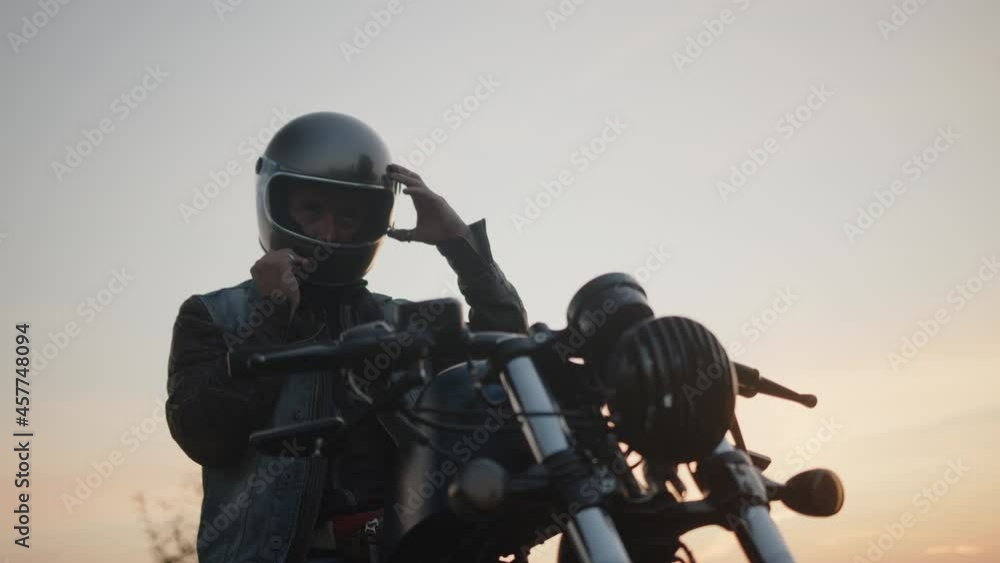 A motorbike rider adjusting his helmet with the sunset sky in the background. A motorbike rider adjusting his helmet with the sunset sky in the background.