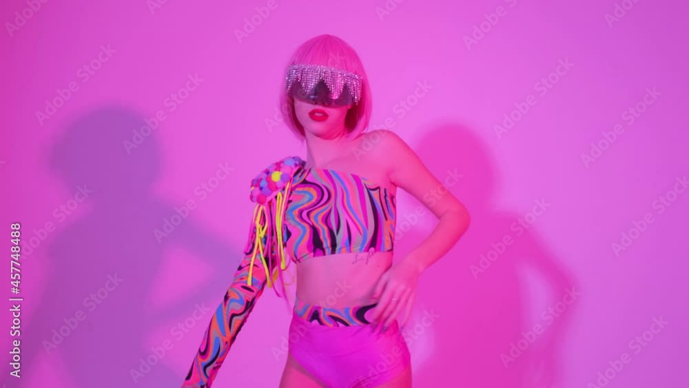 Portrait of a girl in creative glasses in pink trendy neon light. The woman dances and moves gracefully to the club music. Portrait of a girl in creative glasses in pink trendy neon light. The woman dances and moves gracefully to the club music.