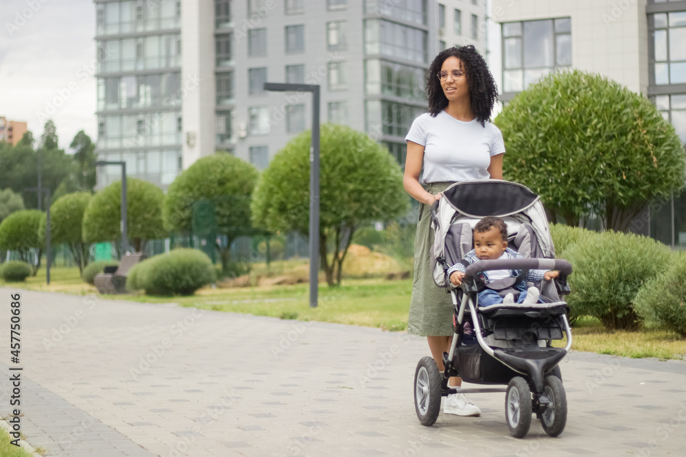 A young black mother walks with her child, who is sitting in a stroller