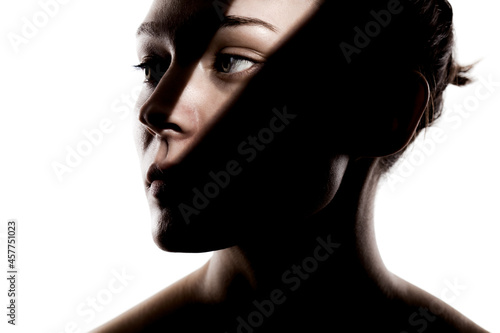 Fashionable studio portrait of a cute girl. Silhouette of a beautiful young woman with hard shadows on her face against white backgroung.