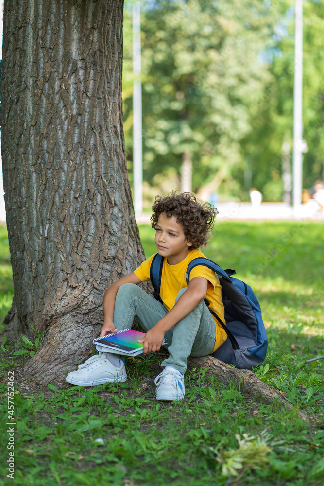A schoolboy with curly hair sits in his hands in the hands of a notebook A schoolboy with curly hair sits in his hands in the hands of a notebook