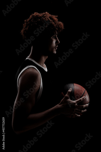 Professional basketball player holding a ball against black background. Serious concentrated african american man in sports uniform