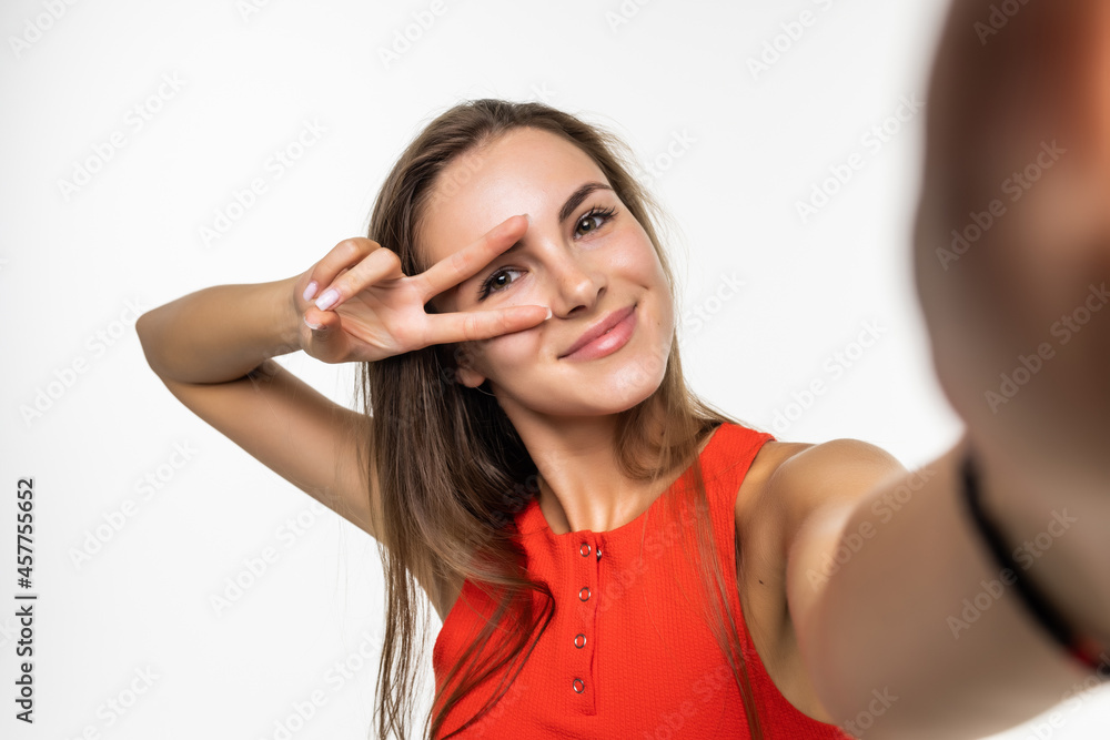 Obraz premium Portrait of a happy young woman making funny face while taking pictures of herself over white background
