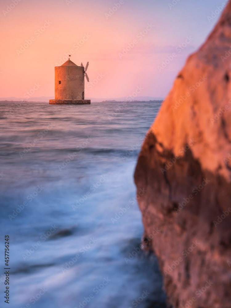 silk water with view to old windmill at sea through orange stone on the beach  in Orbetello in Tuscany in Italy