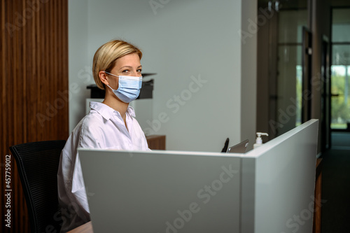 Business administrative worker. Receptionist workplace during pandemic. Female wearing protective mask at workplace. Female short hair blonde secretary. Office manager at work. Customer support desk. 