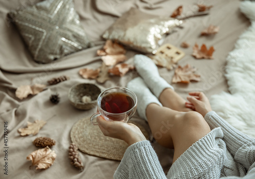 Glass cup of tea in a female hand on a blurred background with autumn leaves.