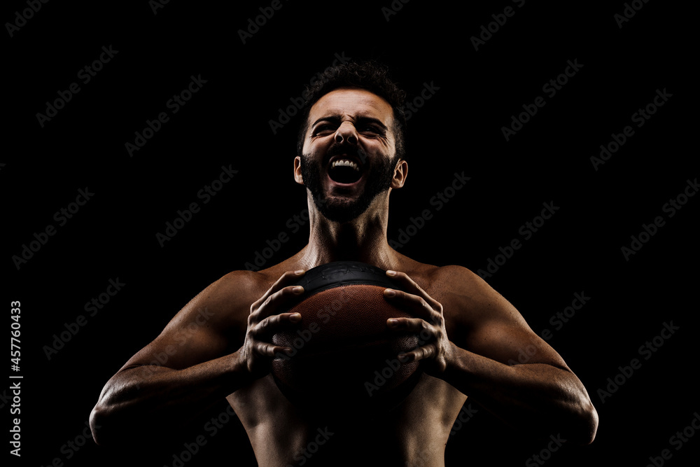 Basketball player holding a ball against black background. Side lit muscular Caucasian man silhouette