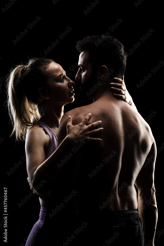 Fit couple posing together. Boy and girl side lit silhouettes on black background. Fit couple posing together. Boy and girl side lit silhouettes on black background.