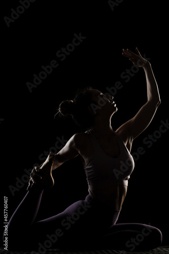 Fit girl practicing yoga in a studio. Half silhouette side lit fitness model. © Nikola Spasenoski