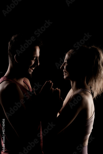 Fit couple posing together. Boy and girl side lit silhouettes on black background. © Nikola Spasenoski