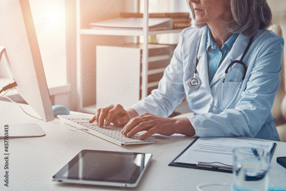 Close up of female doctor in white lab coat working using computer while sitting in her office Close up of female doctor in white lab coat working using computer while sitting in her office