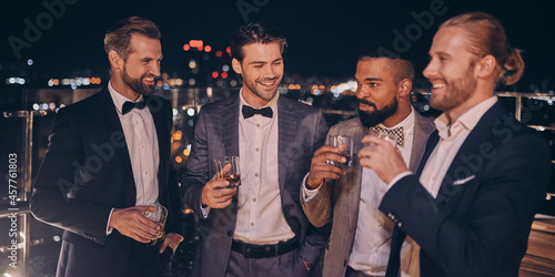 Group of handsome young men in suits and bowties drinking whiskey and smiling photo
