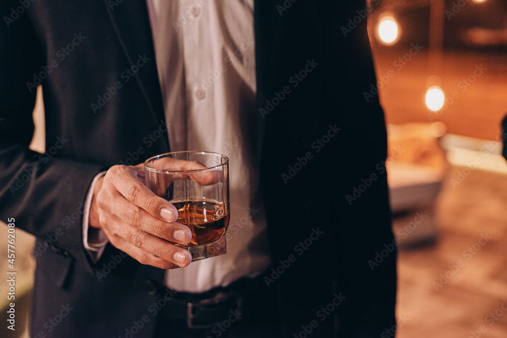 Close-up fo man in black suit holding glass with whiskey