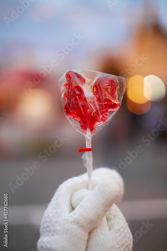 Lollipop in the shape of a rooster in hands against the background of New Year's lights. Bokeh. Blurred background