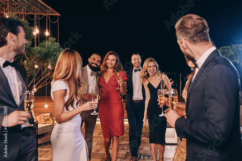 Group of beautiful people in formalwear communicating and smiling while spending time on luxury party