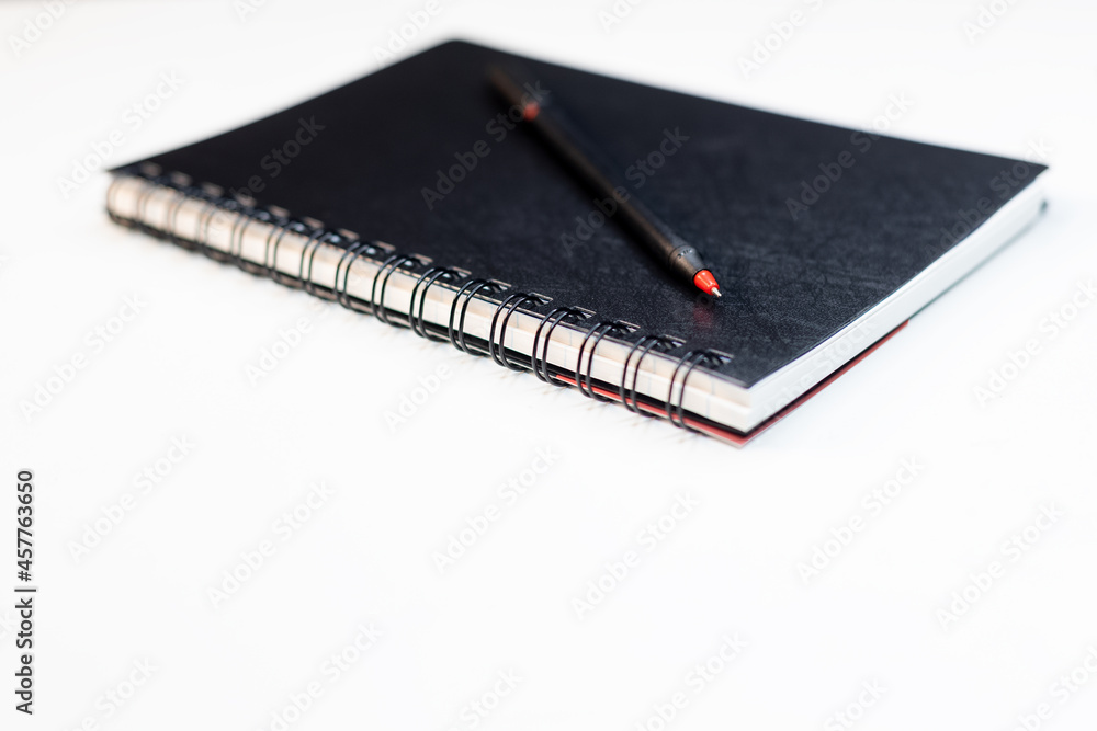 view of closed black cover spiral binding notebook with pen isolated on white desk background partial focus blurred background view of closed black cover spiral binding notebook with pen isolated on white desk background partial focus blurred background