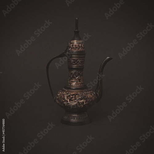 Vintage traditional islamic oriental engraved pitcher handmade on dark background. Elegant arabian antique tall metal jug. photo