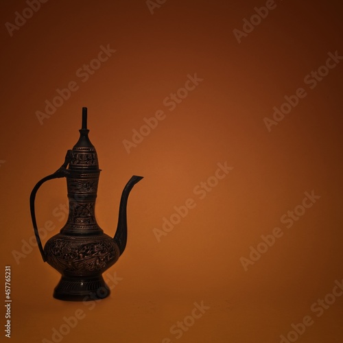 Vintage traditional islamic oriental engraved pitcher handmade on dark orange background. Elegant arabian antique tall metal jug. photo