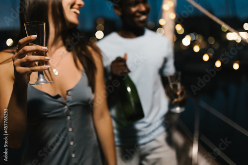 Biracial couple having party and dancing with friends while drinking champagne and celebrating new year eve - Focus on glass photo