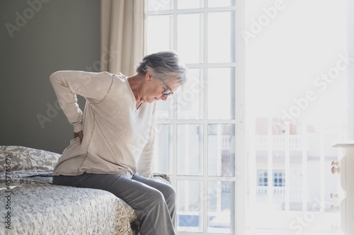 Foto Tired senior woman suffering from backache after sleep, rubbing stiff muscles, O
