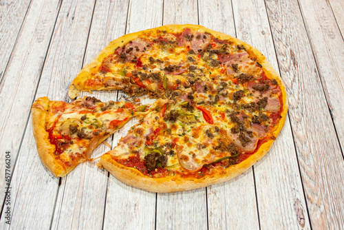 Pizza with minced meat, red peppers, slices of smoked bacon, tomato and oregano with onion and mozzarella cheese