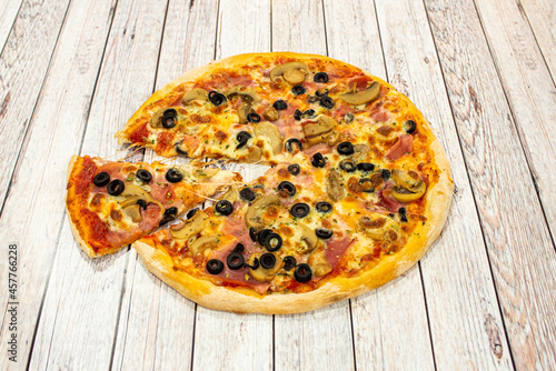 Small thin crust pizza with slices of black olives, slices of mushroom, cooked ham, oregano and a portion stretching the melted mozzarella cheese