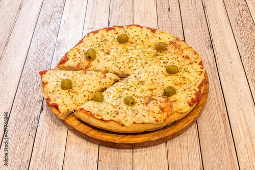 Pizza with lots of melted cheese and tomato, oregano with green pitted olives on wooden plate