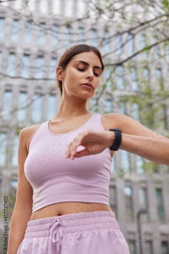 Blurry image of sporty woman has broadwalk in city during daylight checks health state and workout activity on smartwatch dressed in activewear poses outdoor monitots heart beat after fitness