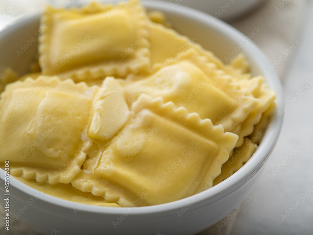 White bowl with delicious Italian ravioli. On top of them is a piece of butter. White background. Macro photography. Restaurant, hotel, home cooking, recipe book, dish design. White bowl with delicious Italian ravioli. On top of them is a piece of butter. White background. Macro photography. Restaurant, hotel, home cooking, recipe book, dish design.