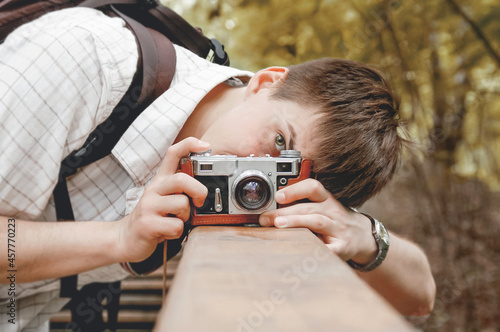 Young man takes a shoot with old fashioned film camera. Handsome man in autumn park. Photographer with retro photo camera. Fall season. photo