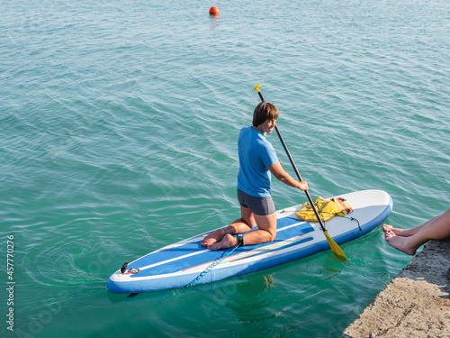 Handsome paddle boarder. Sportsman on knees paddling on stand up paddleboard. SUP surfing. Active lifestyle. Outdoor recreation. Vacation on seaside.