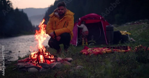 man watching the bonfire while capming with family in mountains near the river. active leisure photo