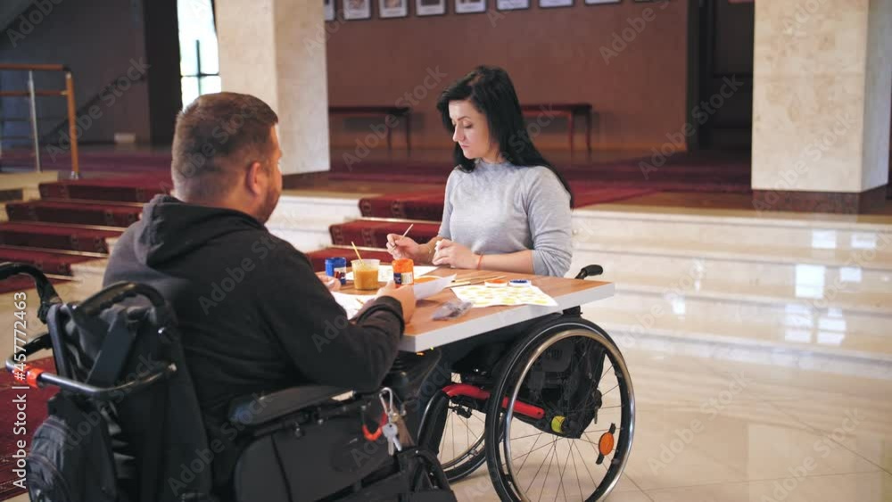 wheelchair. disability. disabled young man and woman are drawing with paints, sitting in wheelchairs at table. creative group lessons for people with disabilities. Education, relationship and humanity wheelchair. disability. disabled young man and woman are drawing with paints, sitting in wheelchairs at table. creative group lessons for people with disabilities. Education, relationship and humanity