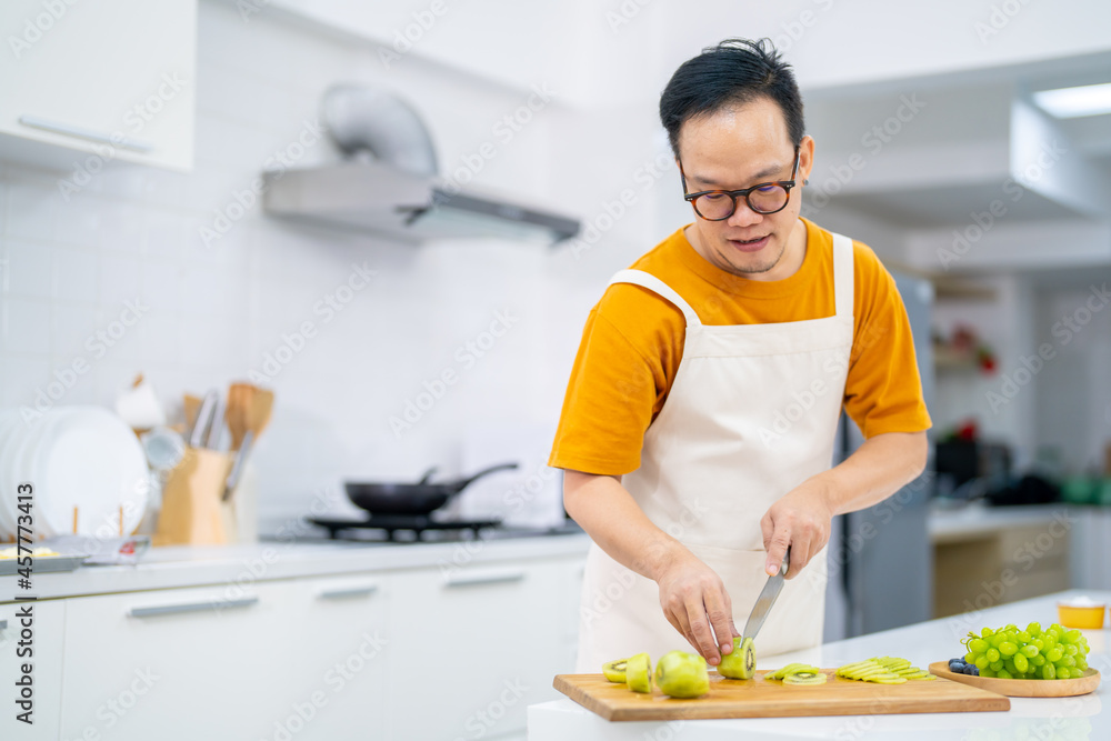 Asian man bakery shop owner preparing bakery in the kitchen. Male pastry chef using kitchen knife cut fresh fruit for making fruit tart. Small business entrepreneur and indoor lifestyle baking concept