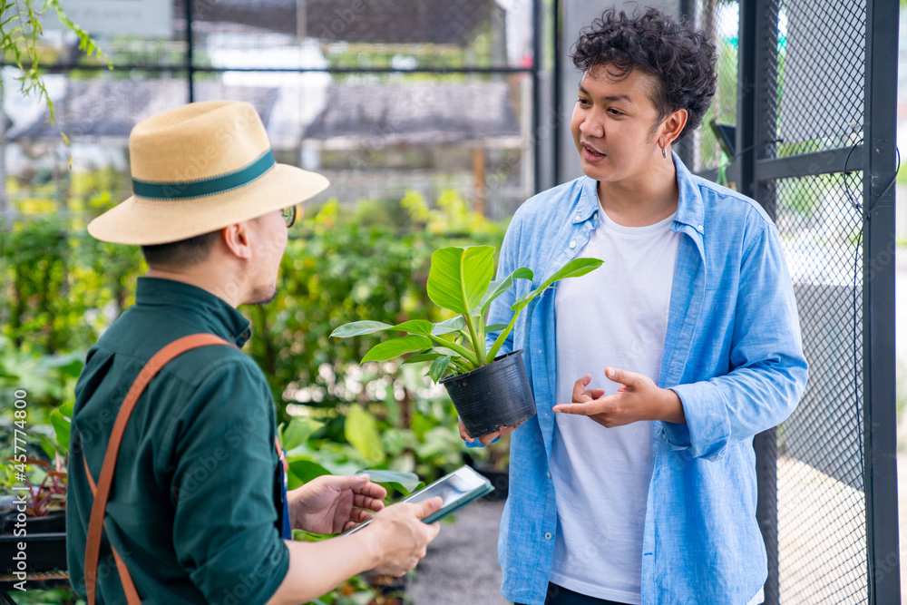 Asian man plant shop owner help customer choosing potted plants in greenhouse garden. Handsome male buying plant and flower for growing at home. Small business and indoor activity lifestyle concept Asian man plant shop owner help customer choosing potted plants in greenhouse garden. Handsome male buying plant and flower for growing at home. Small business and indoor activity lifestyle concept