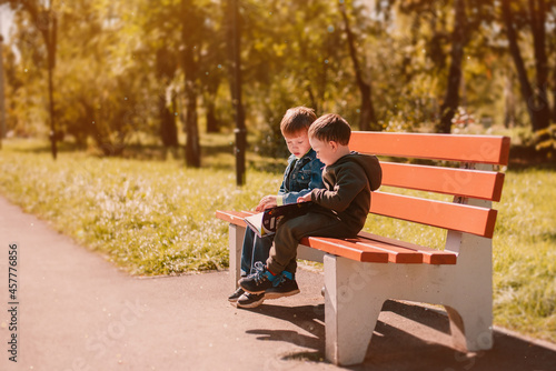Autumn September, two boys reading a book on a park bench, warm, golden autumn