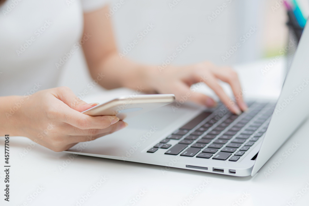 Closeup hand of young woman working laptop computer and reading smartphone on internet online on desk at home, freelance girl using phone with social media, business and communication concept. Closeup hand of young woman working laptop computer and reading smartphone on internet online on desk at home, freelance girl using phone with social media, business and communication concept.