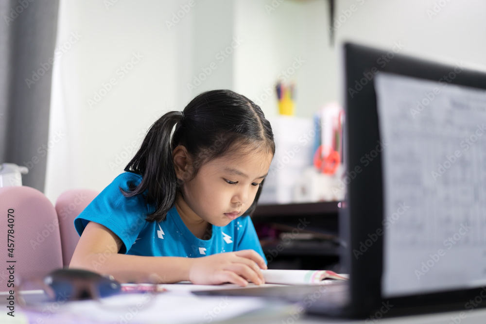 Asian child student or kid girl reading on book to learning and studying online class on computer notebook or person learn from home by video call on laptop for back to school by homeschool education Asian child student or kid girl reading on book to learning and studying online class on computer notebook or person learn from home by video call on laptop for back to school by homeschool education