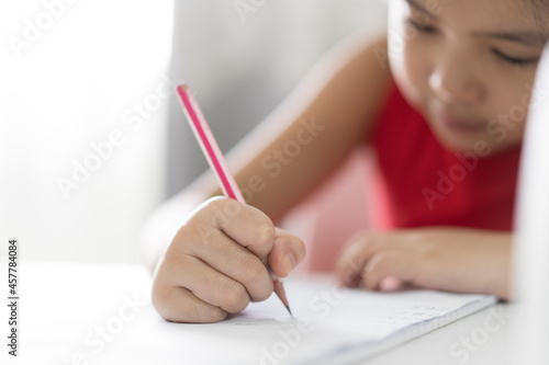 closeup hand of asian child or kid girl enjoy writing or draw learning and doing homework or person learn from home and practicing write by pencil on paper book and study online from back to school