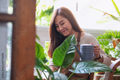 A young woman taking care and watering houseplants by watering can at home
