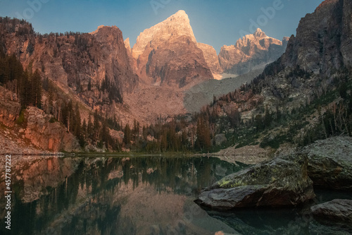 View of Delta Lake in Grand Teton National Park, Wyoming at sunrise with the mountain peak lit up pink from the sun.