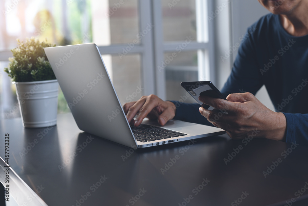 Casual business man using mobile phone and working on laptop computer at home office, work from home concept Casual business man using mobile phone and working on laptop computer at home office, work from home concept