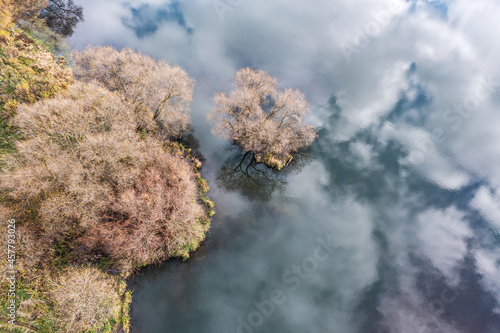 picturesque autumn lake landscape. small island with bare trees on calm water surface with clouds reflections. aerial overhead view.