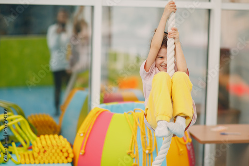Fototapeta Naklejka Na Ścianę i Meble -  Kids doing exercises climbing tightrope in gym at kindergarten or elementary school. Children sport and fitness concept
